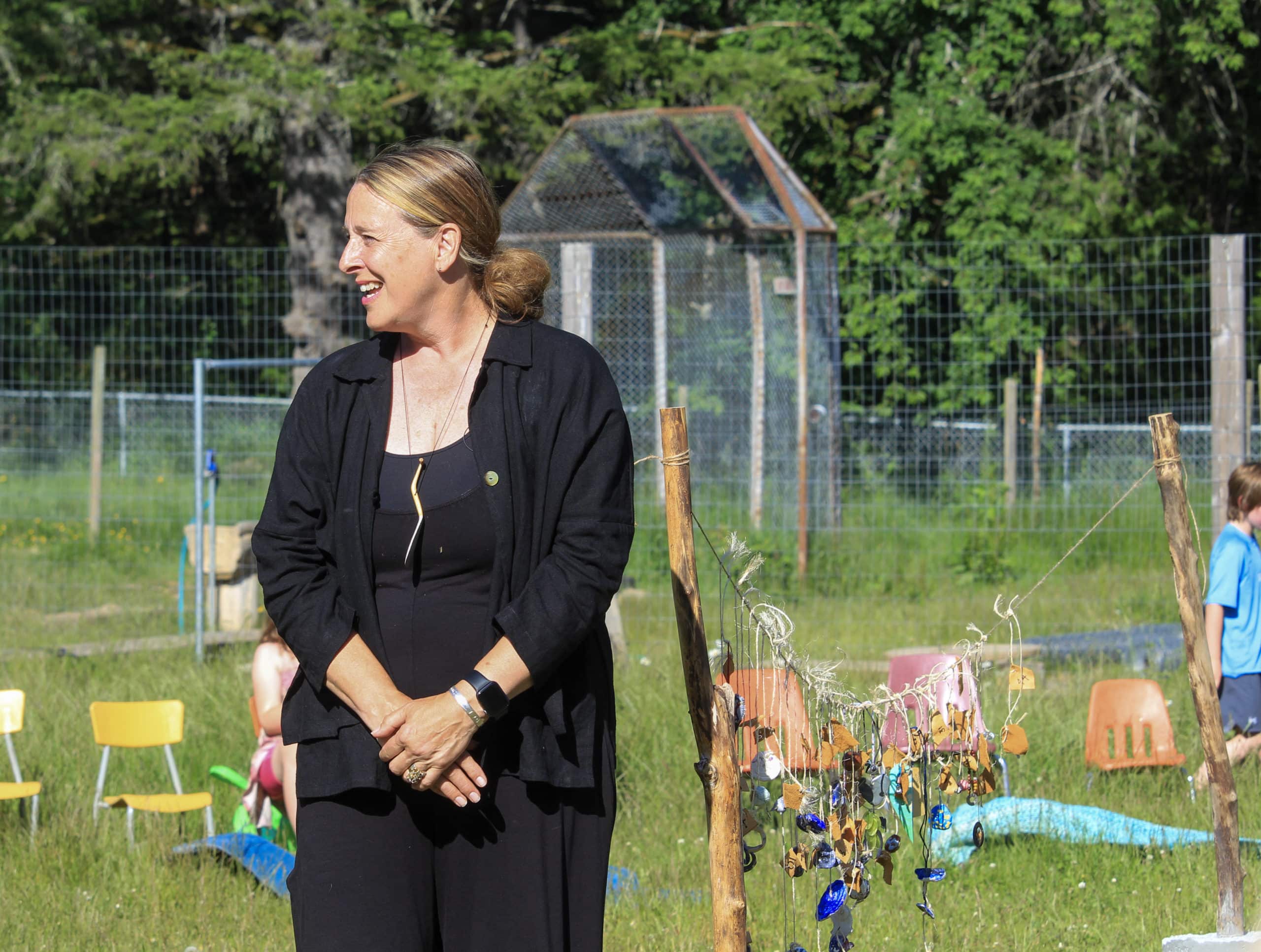 Kim Ondrik stands, hands crossed in front of her, in front of the string of objects at the centre of the chair circle.