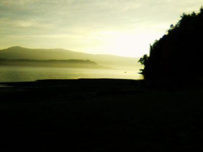 Image shows a coastline with a sharp contrast between dark land and light water and sky.