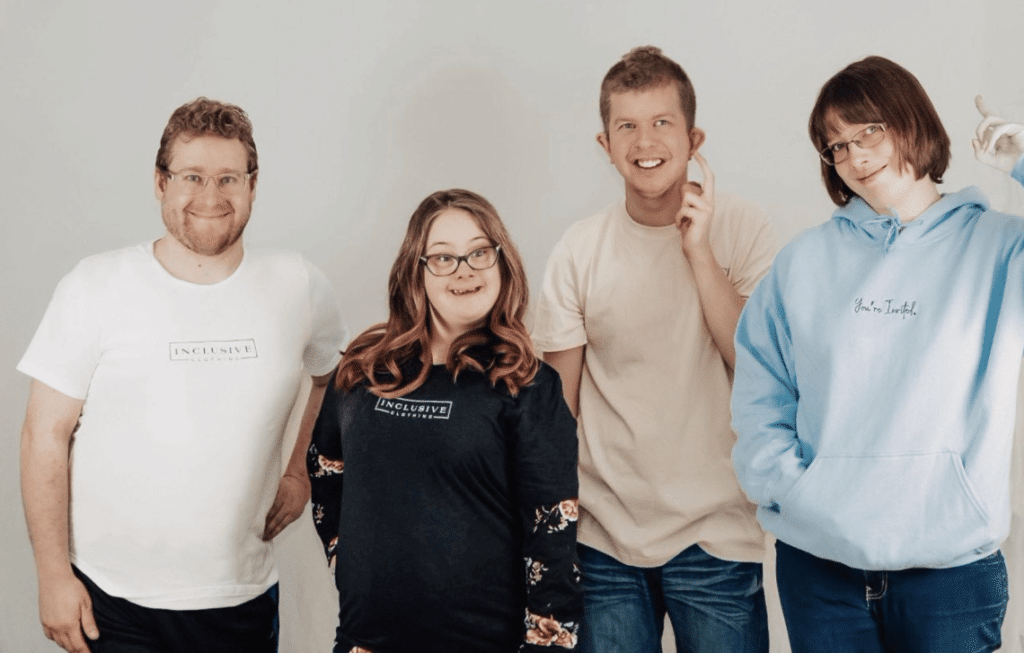 Four models stand in a row wearing inclusive clothing T-shirts and baby blue sweatshirt.