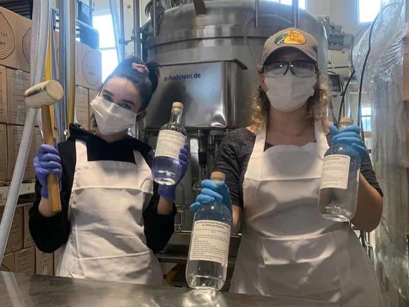 Photo of two women wearing masks and holing up bottles of clear liquid. They offered volunteer help for the COVID-19 coronavirus response.