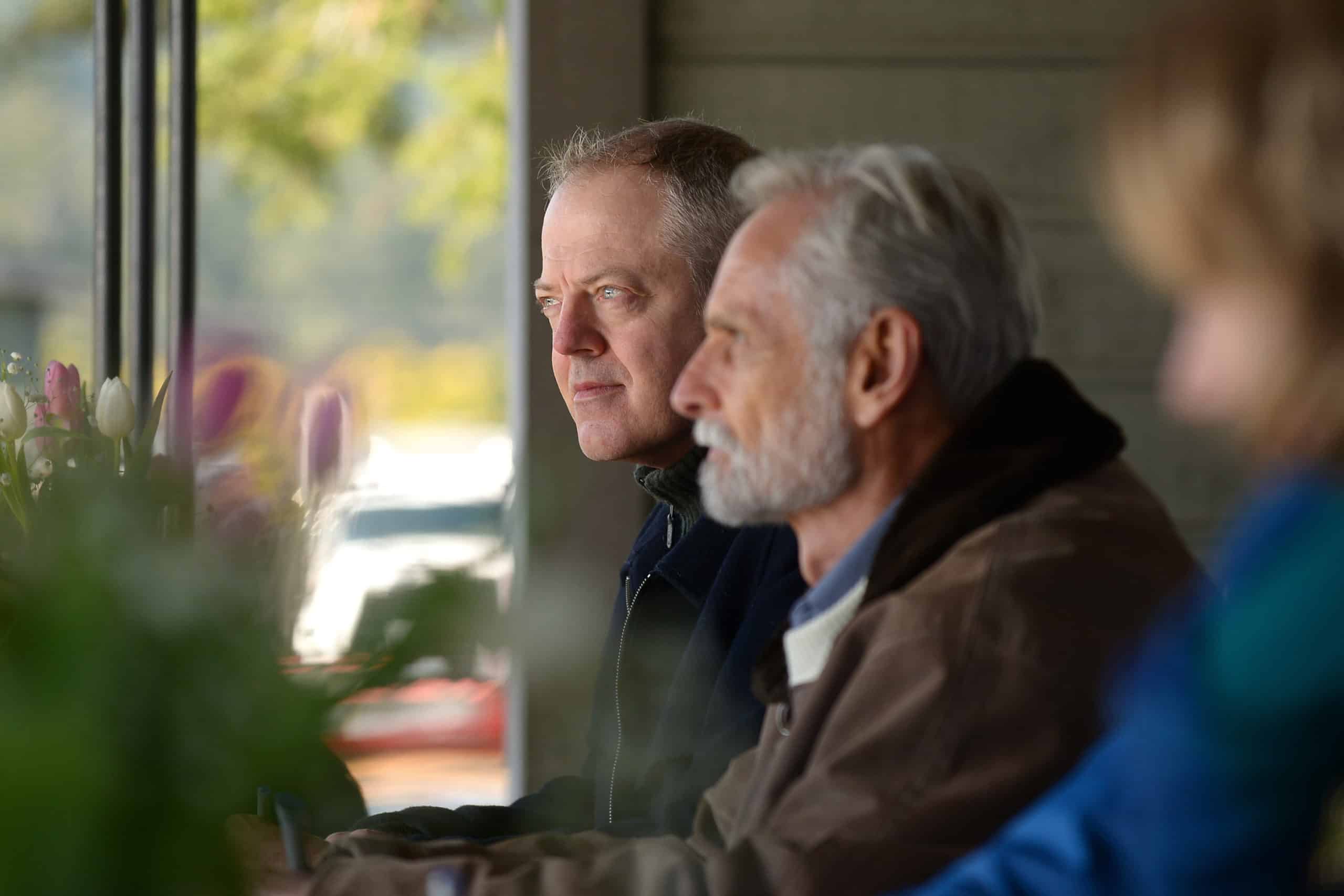 Craig Davis, president of Pearson College UWC, sits with Metchosin Mayor John Ranns as they prepare to sign a standstill agreement to consider a proposed Indigenous protected area at Mary Hill. Flowers are blurred in the foreground.