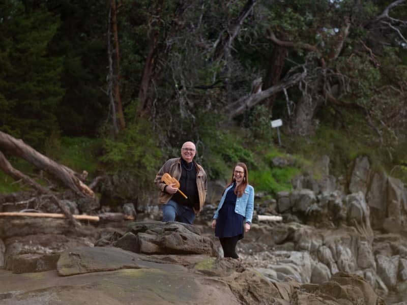 Daniel Elliott and Kim Trotter stand on the rocks at the beach smiling at eachother.