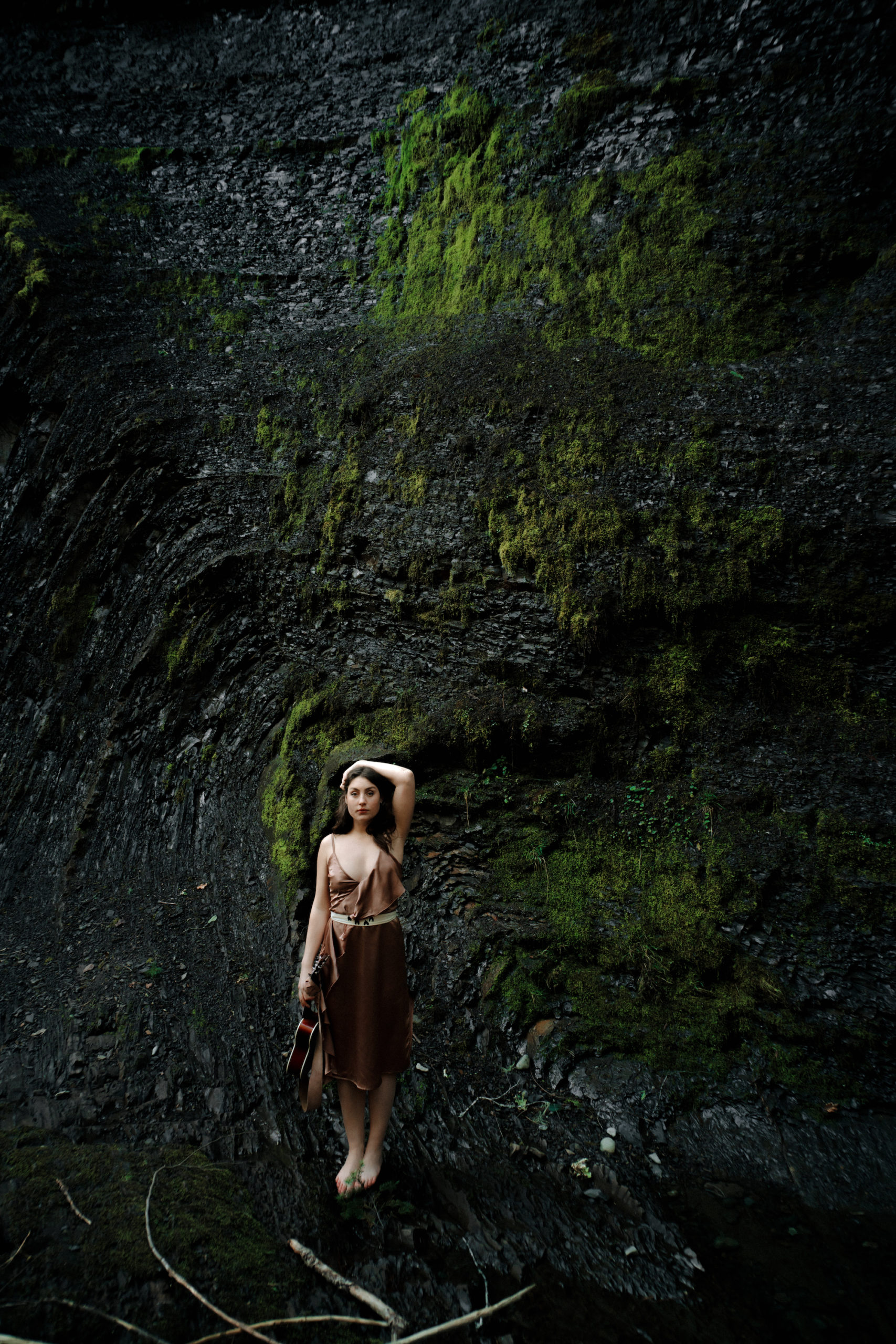 Nanaimo performing artist Elise Boulanger stands in a deep forest green landscape in a flowing dress.