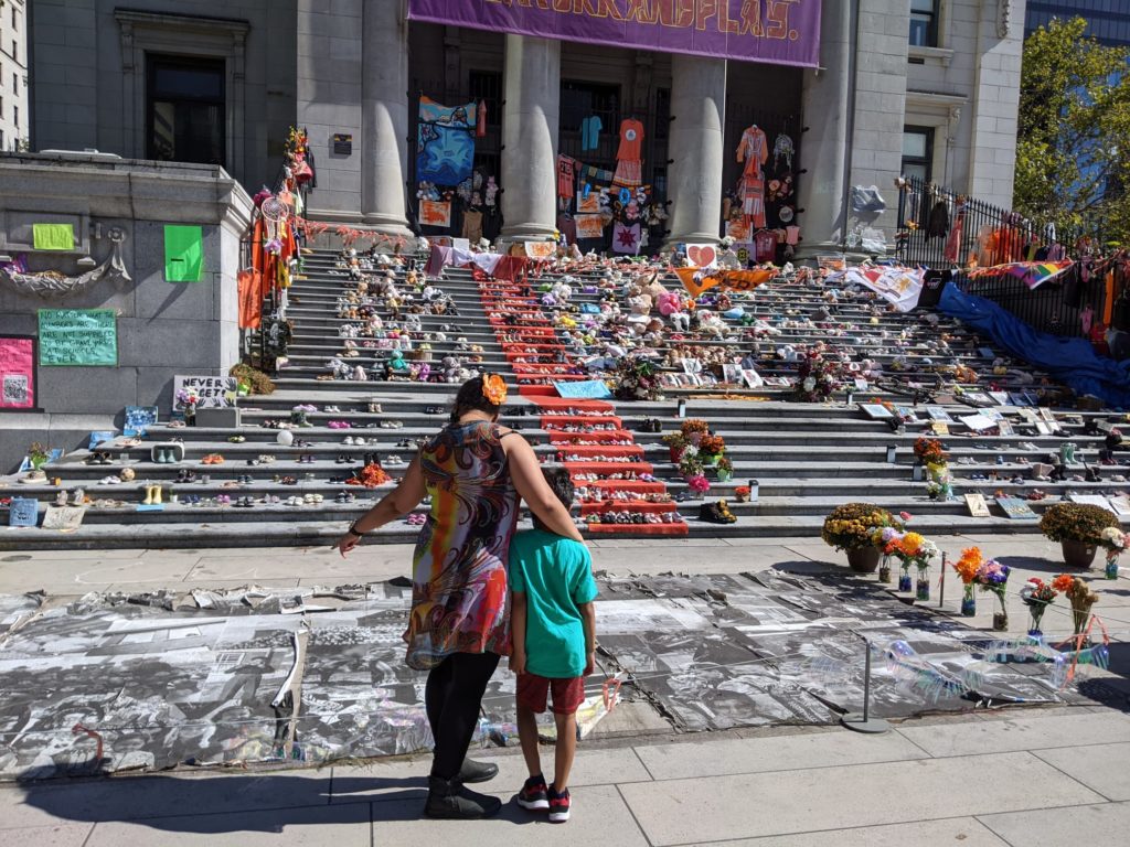 Hina Charania and her son at a memorial for Indigenous children who died at residential "schools." She wears an orange flower in the spirit of reconciliation