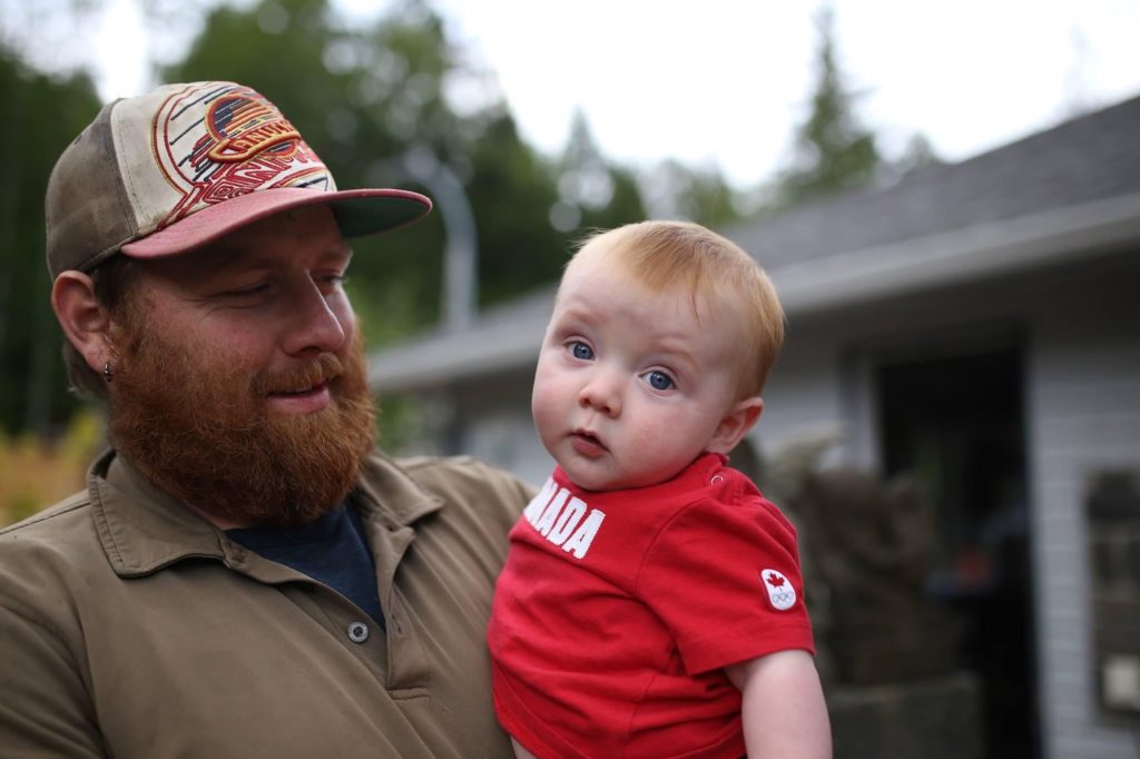 A dad holds his baby boy outside of their house.