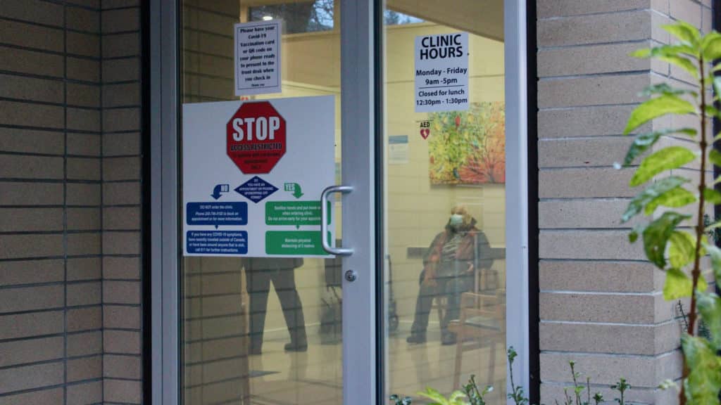 The front glass doors of a doctor's office with signs on it about COVID-19 safety and clinic hours. Cowichan Valley B.C. election candidates have addressed health care in their campaigns.