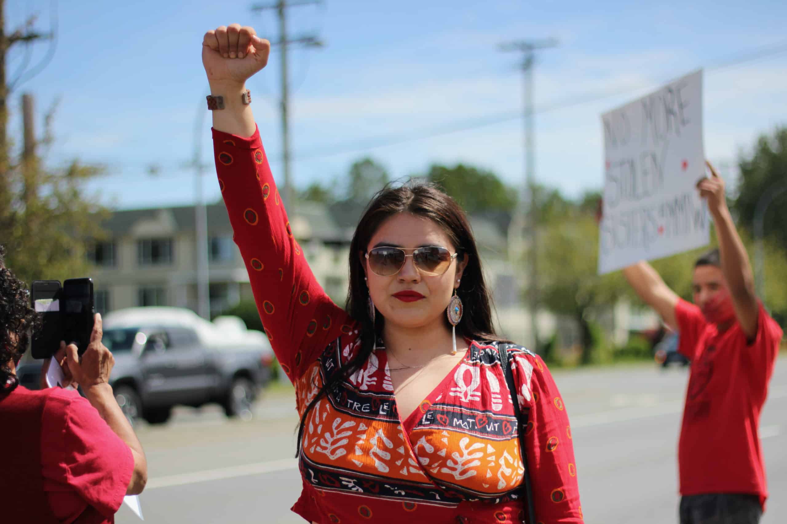 A woman in red raises a fist in a gesture of protest.