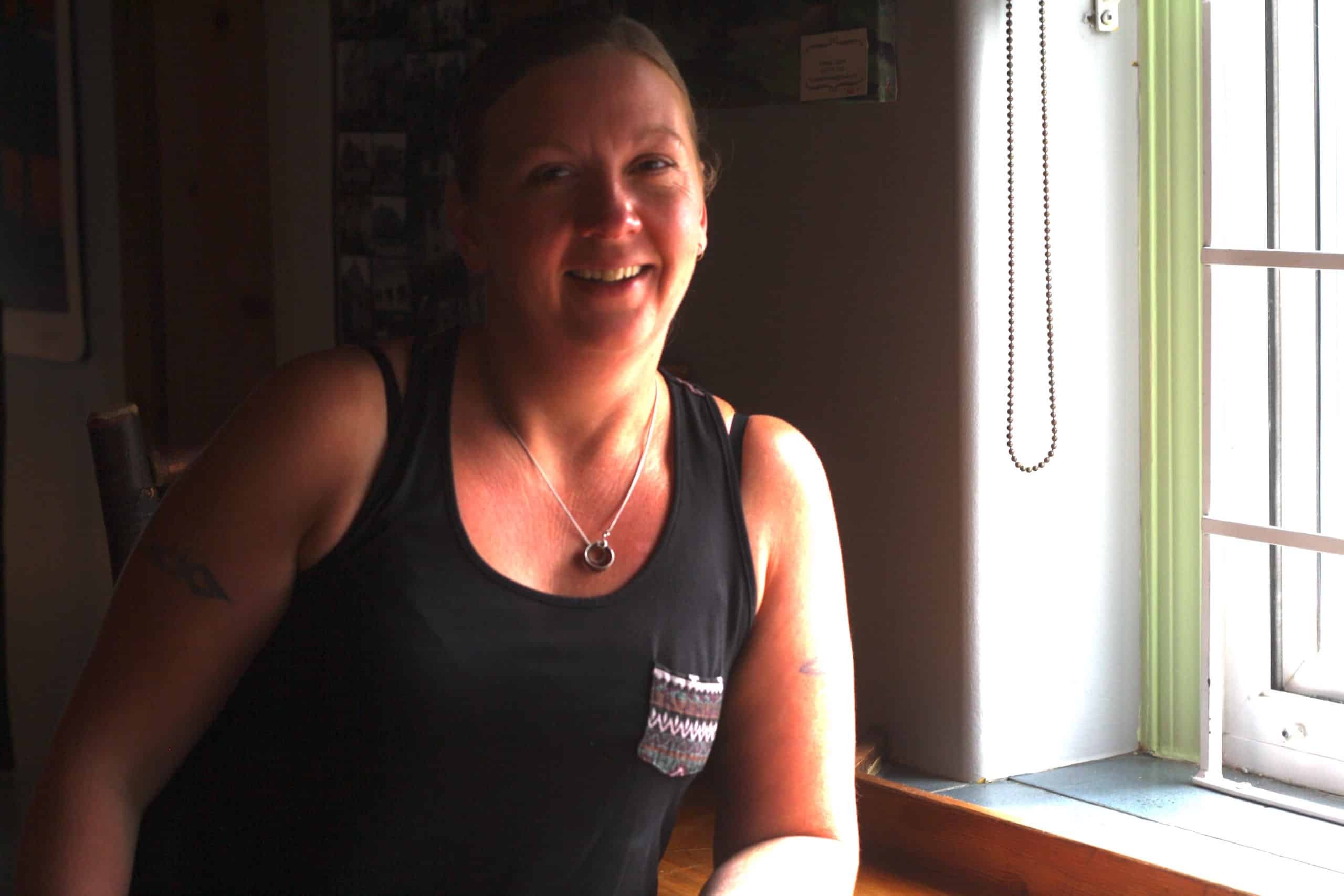 Chrissy Forsythe stands near the window smiling in spite of living with the effects of social disorder at her downtown business.