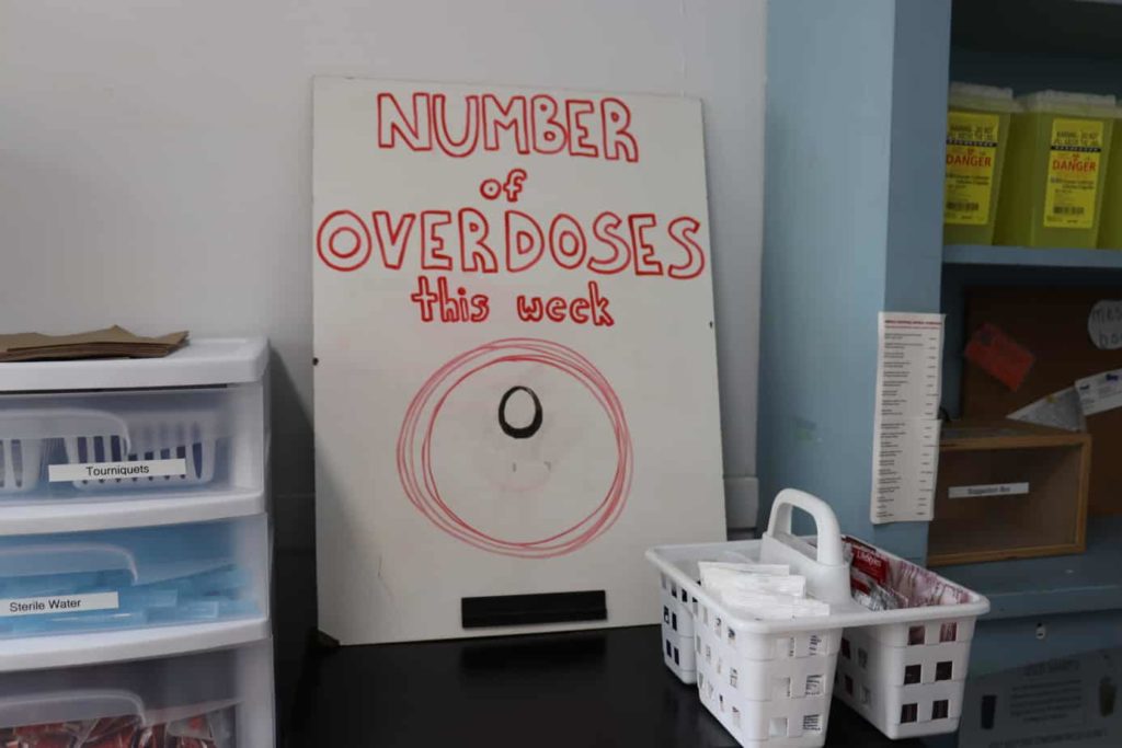 Photo of a white board that says "number of overdoses this week" with a zero below. And medical supplies.