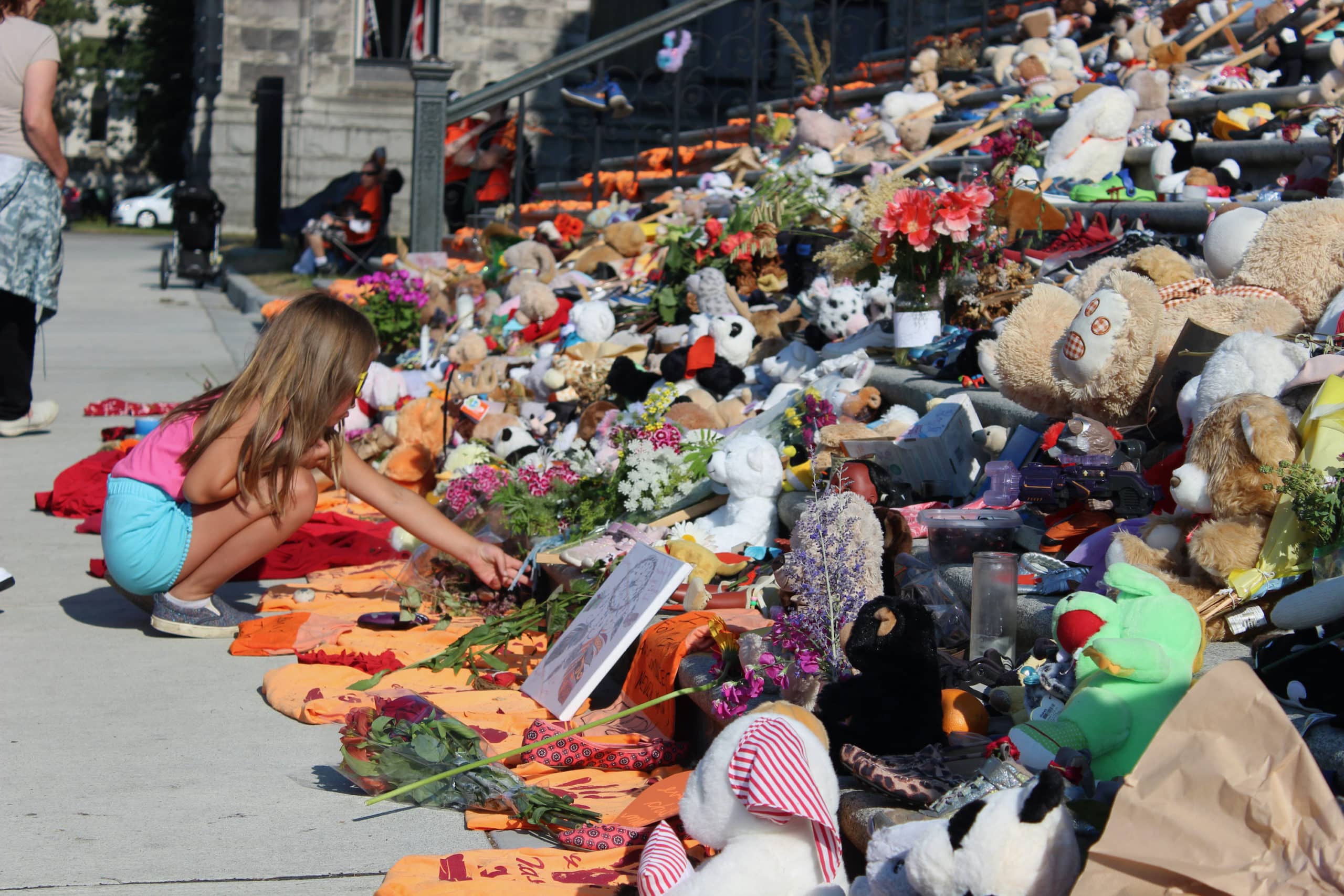 a child crouches in front of steps covered in teddy bears, orange shirts and flowers.