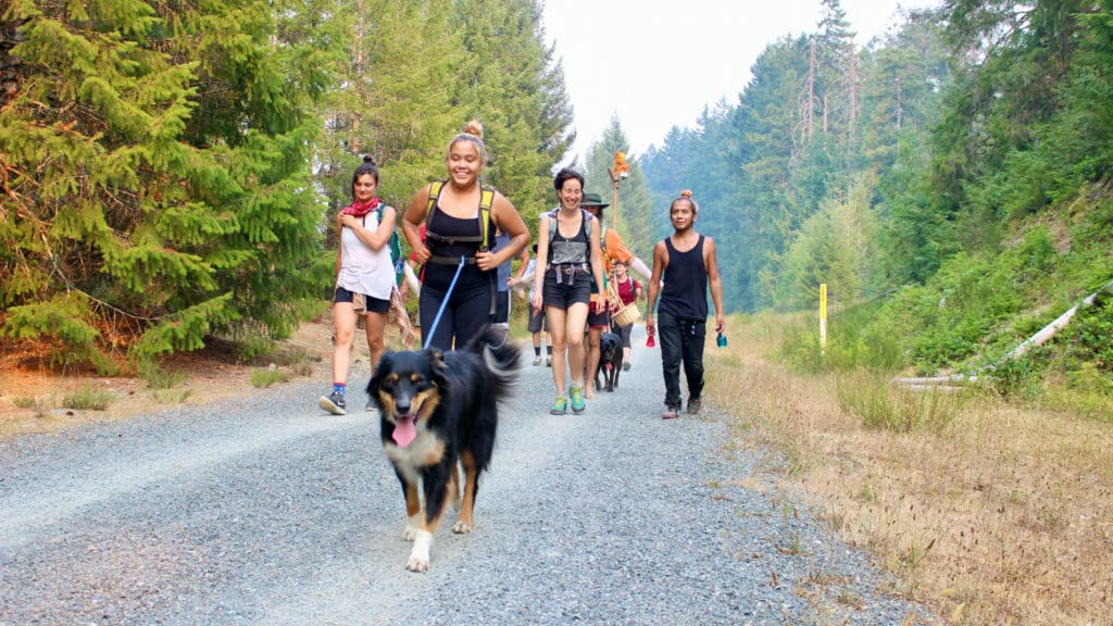 Smiling people walk down a wide trail with a happy dog in front.