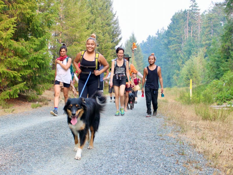 Smiling people walk down a wide trail with a happy dog in front.