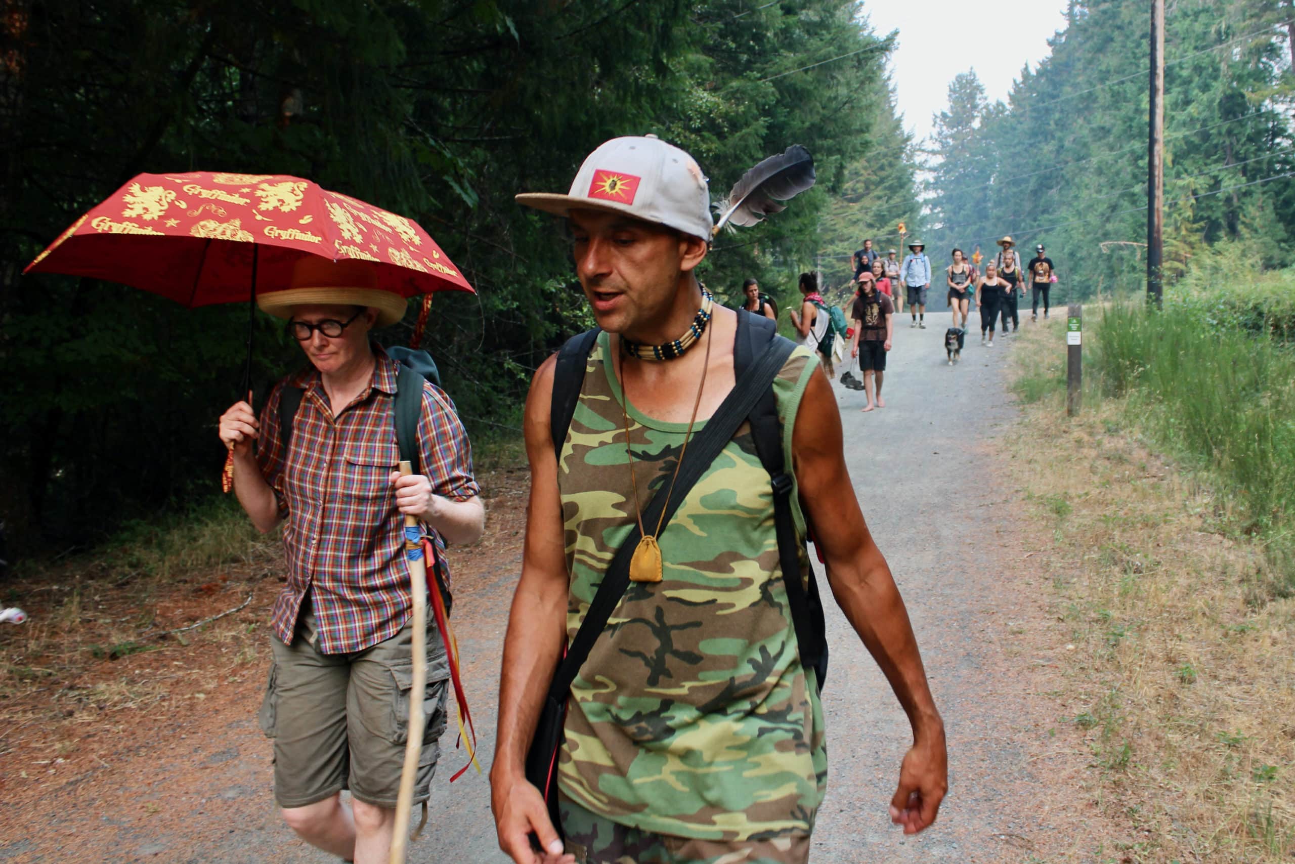 In front, two people walk forward, one carrying an orange umbrella. Others follow on the path behind them. 