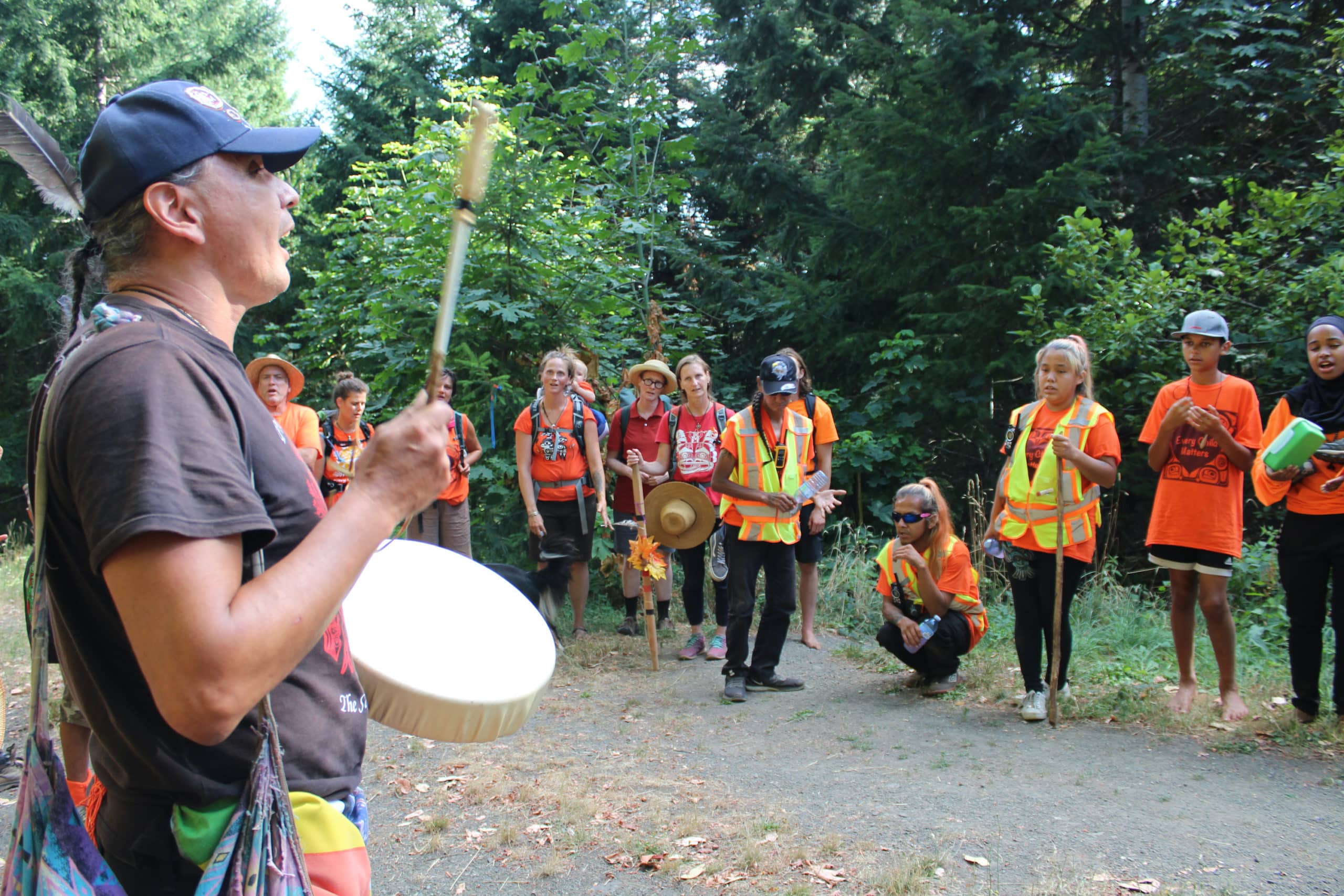 A man drums and signs in a large circle of people.