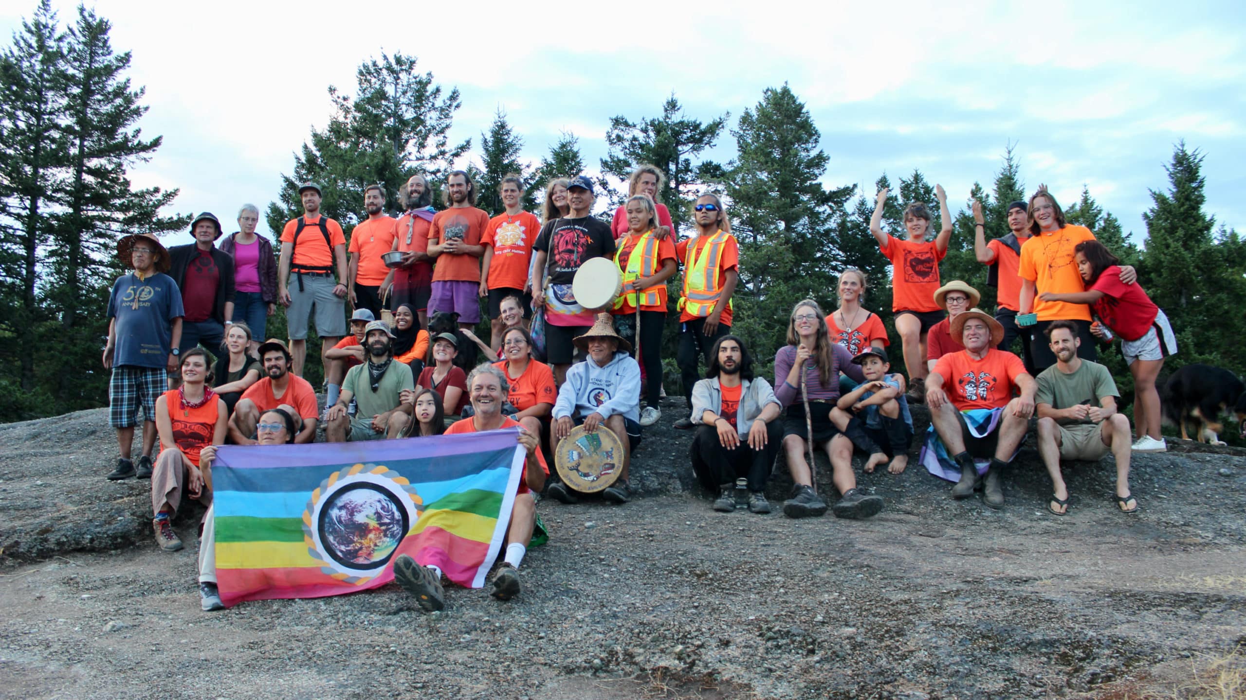About 40 people sit and stand, many wearing orange shirts.