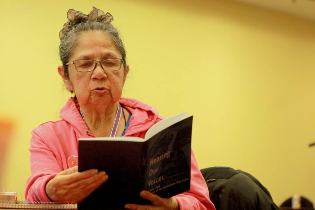 An Elder holds a book and purses her lips to read outloud.