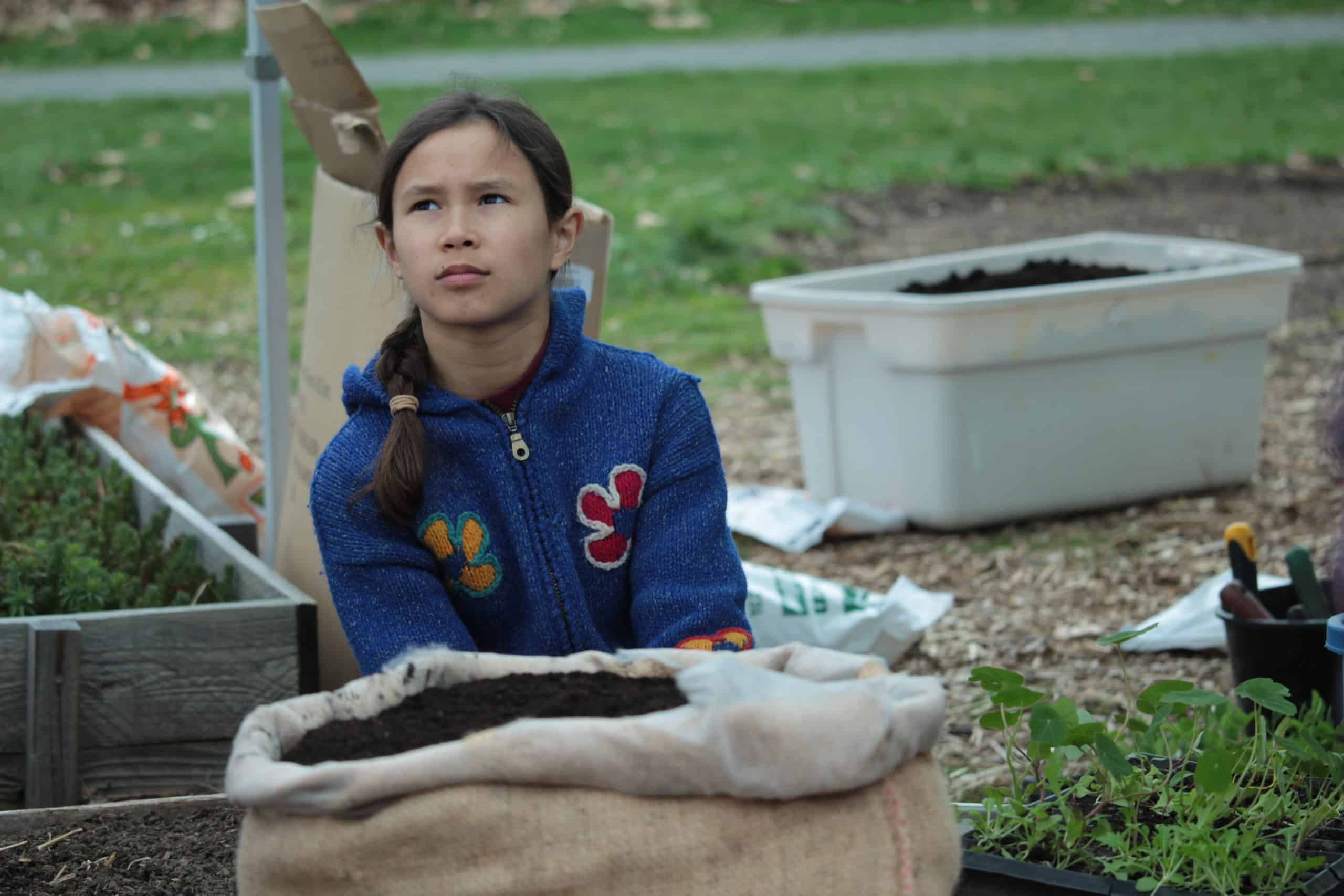 Mila MacDonald-Kee sits with a burlap sack full of soil in front of her.