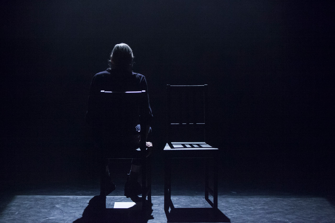A person sits on a dark stage facing away from the camera.