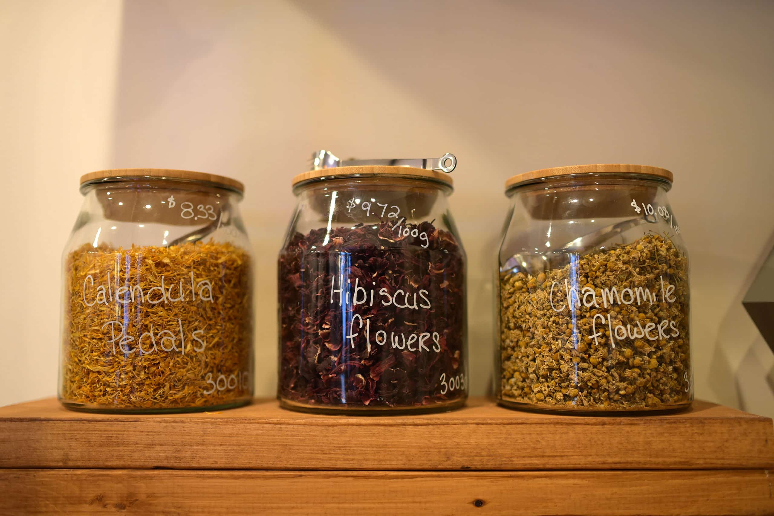Jars of dried calendula petals hibiscus flowers and chamomile flowers sit on a shelf at plentiFILL.