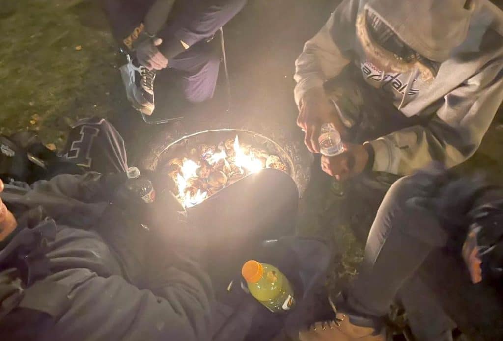 Four people huddle around a propane fireplace, viewed from above.