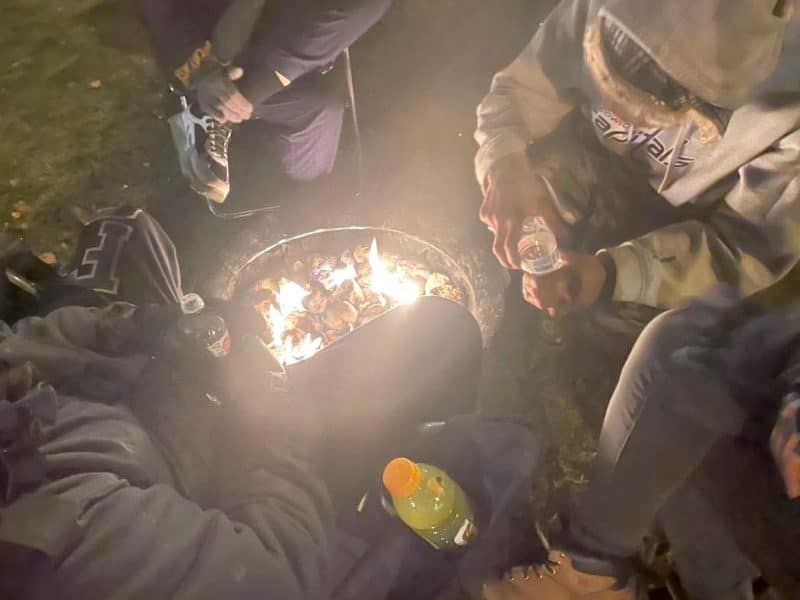 Four people huddle around a propane fireplace, viewed from above.