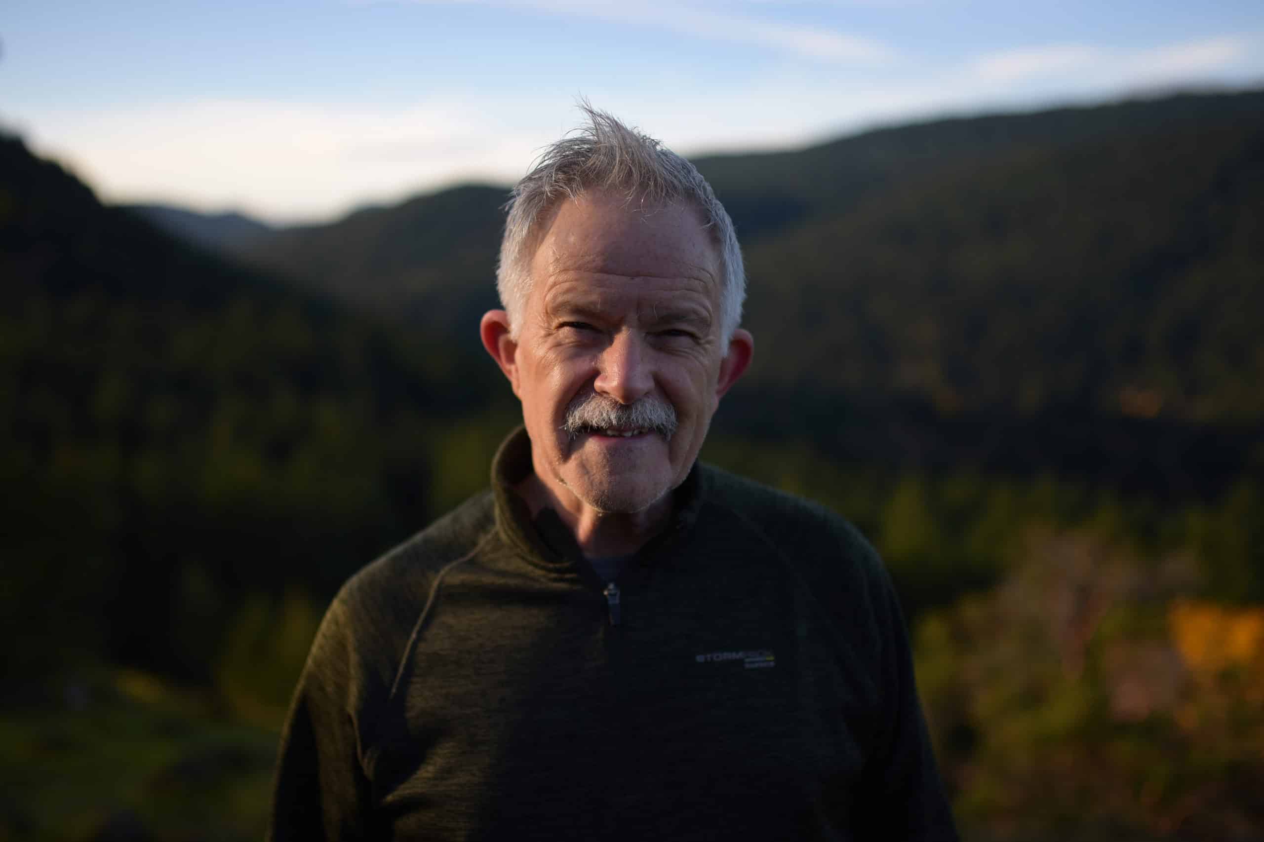 Richard Habgood stands in front of a backdrop of forest and mountains.