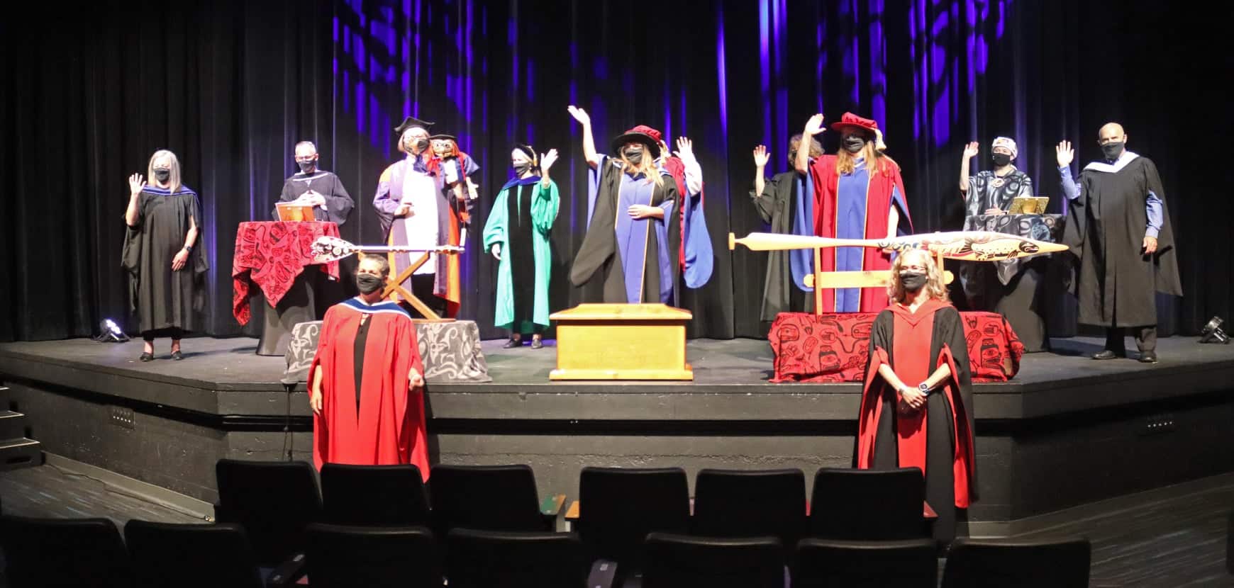 People in academic robes and face masks stand on stage for a COVID-style grads ceremony at VIU 2021.