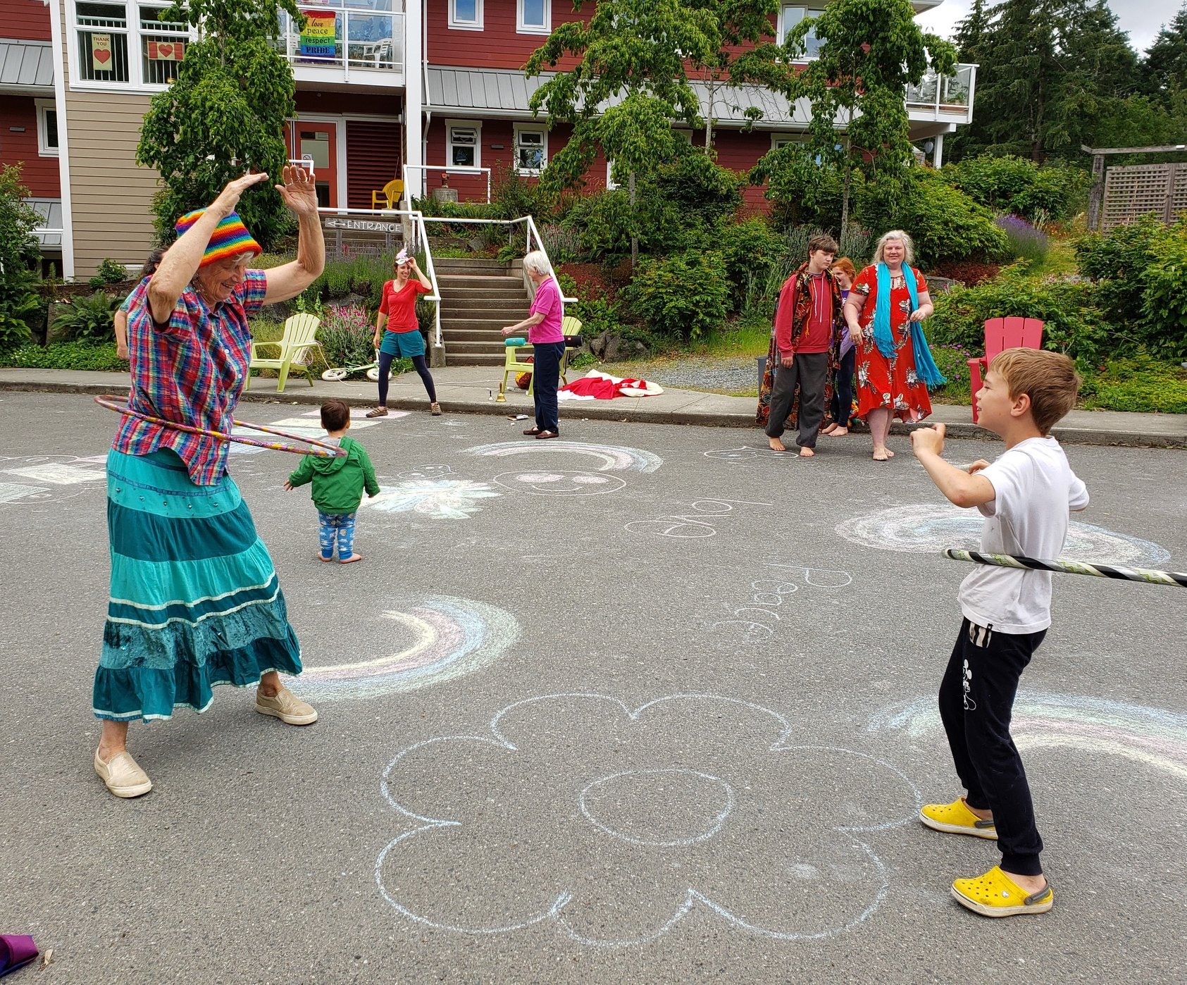 An older person and a young person stand outside facing eachother playing with hulahoops at Nanaimo's only cohousing complex, Pacific Gardens.