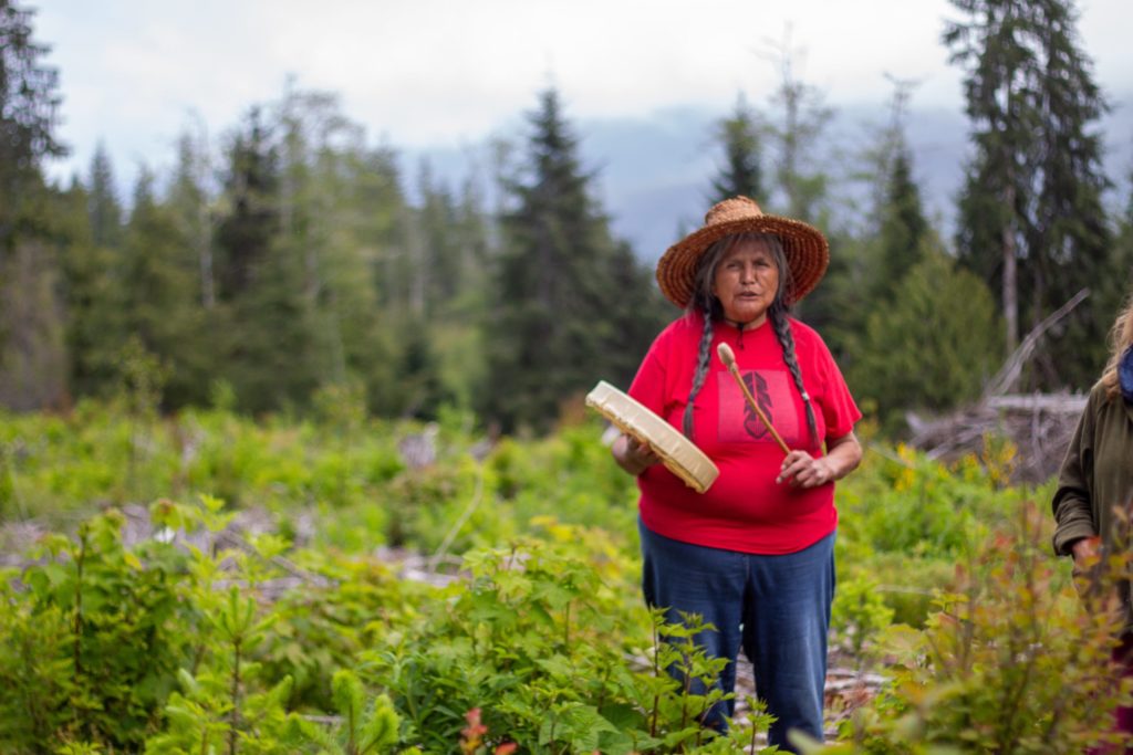 Elder Grandma Rose stands in the forest at Fairy Creek with a drum.