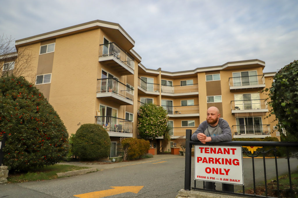 A renter stands in front of a rental unit complex on Prideaux Street in Nanaimo next to a sign that says "tenant parking only."