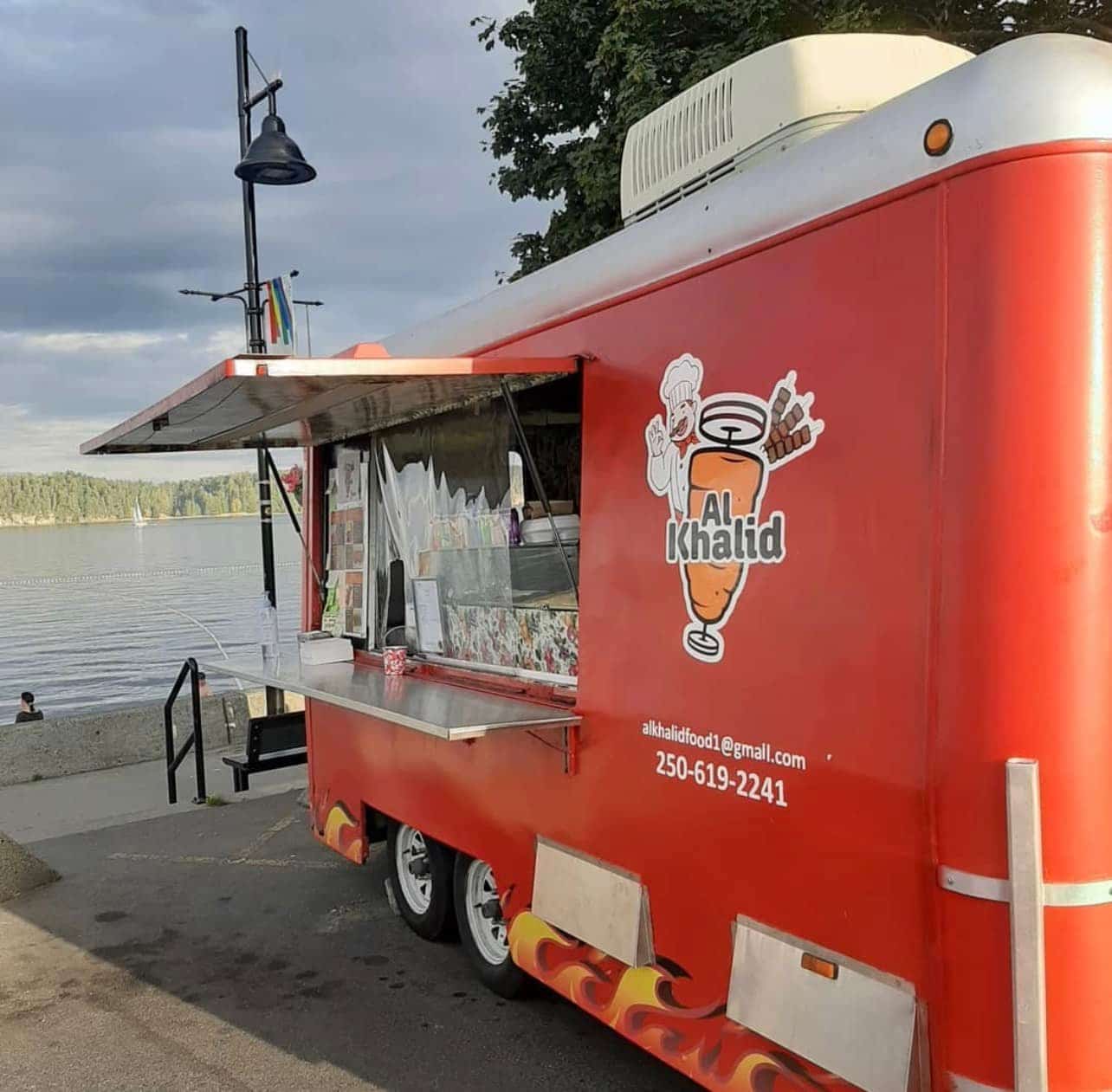A red Shawarma food truck with the words Al Khalid is parked at a beach.