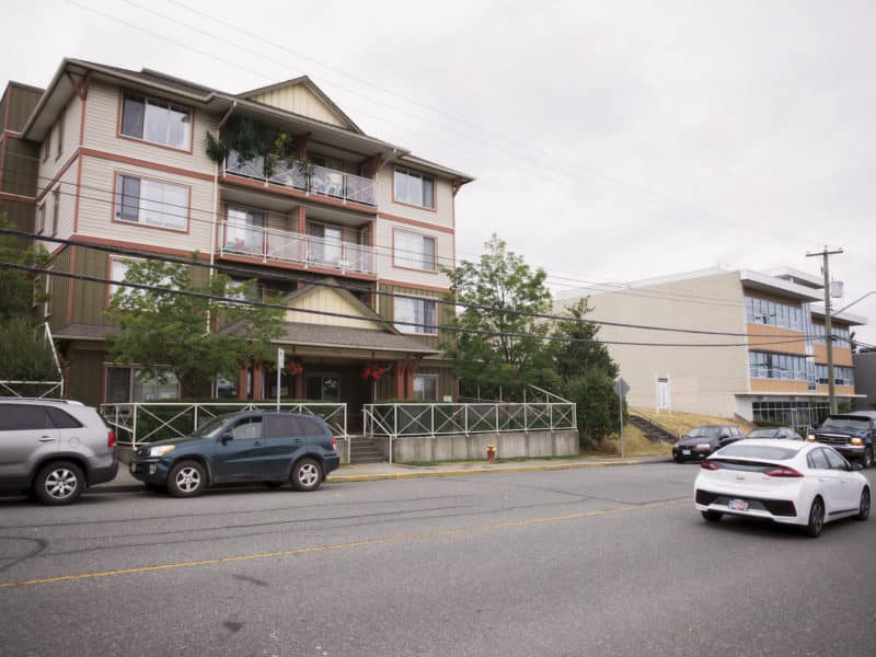 A four storey building stands tall from the opposite side of the street as cars go by.