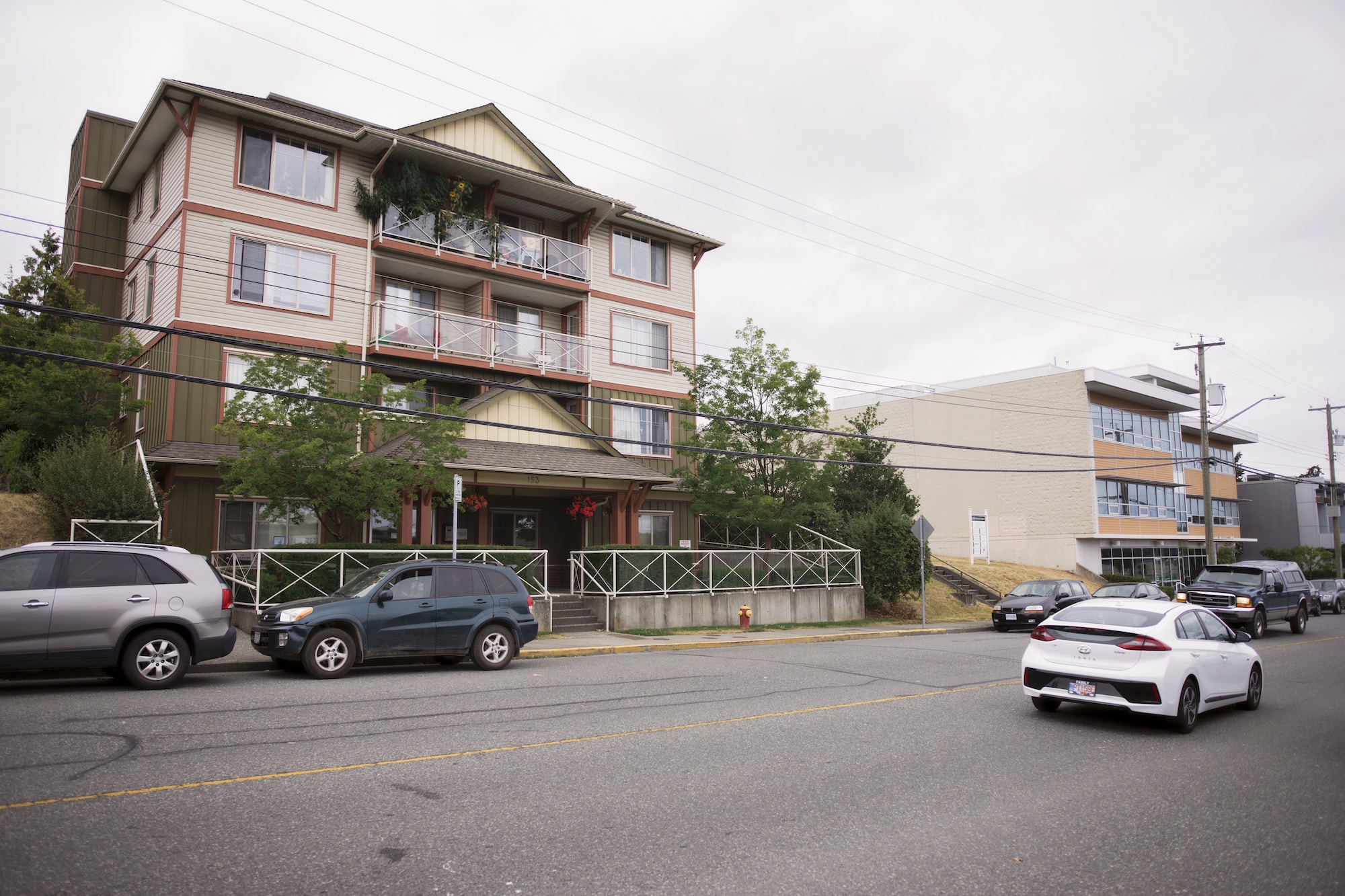A four storey building stands tall from the opposite side of the street as cars go by.