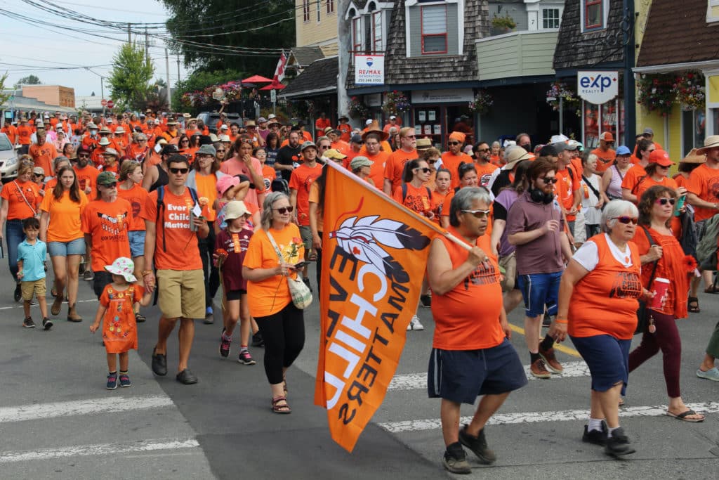 A large crowd dressed in orange shirts marches down a street
