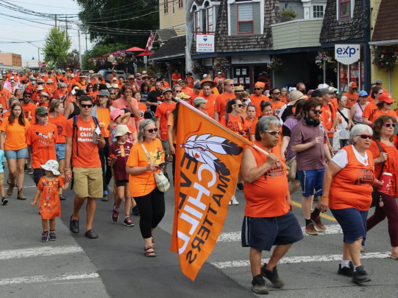 A large crowd dressed in orange shirts marches down a street