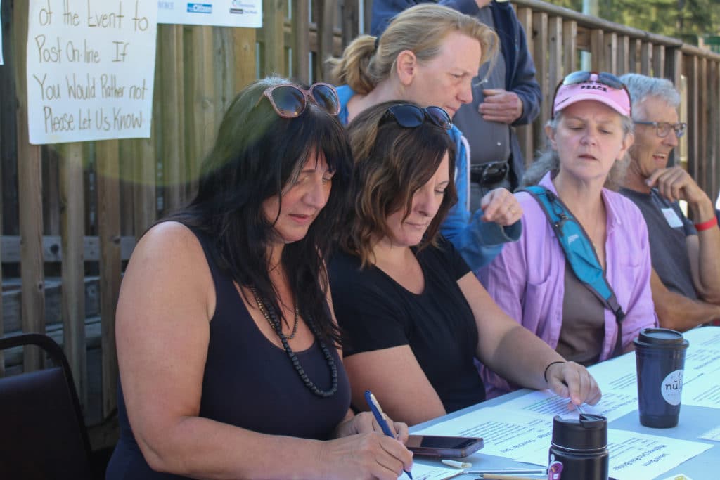 Six people sit and stand behind a table with papers on it