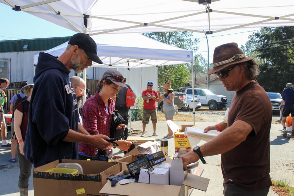 Three people look at boxes of supplies under tents