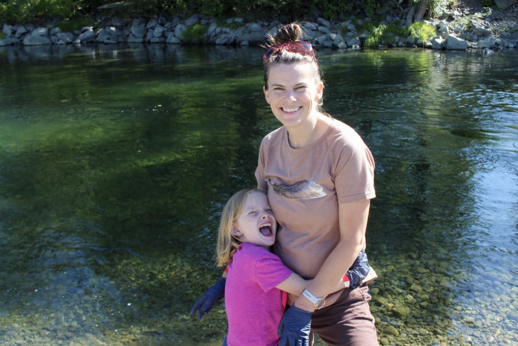 A child smiles broadly and hugs her mom, who is smiling
