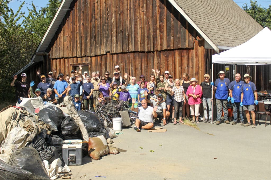 a large group of people stands and waves behind a large pile of trash