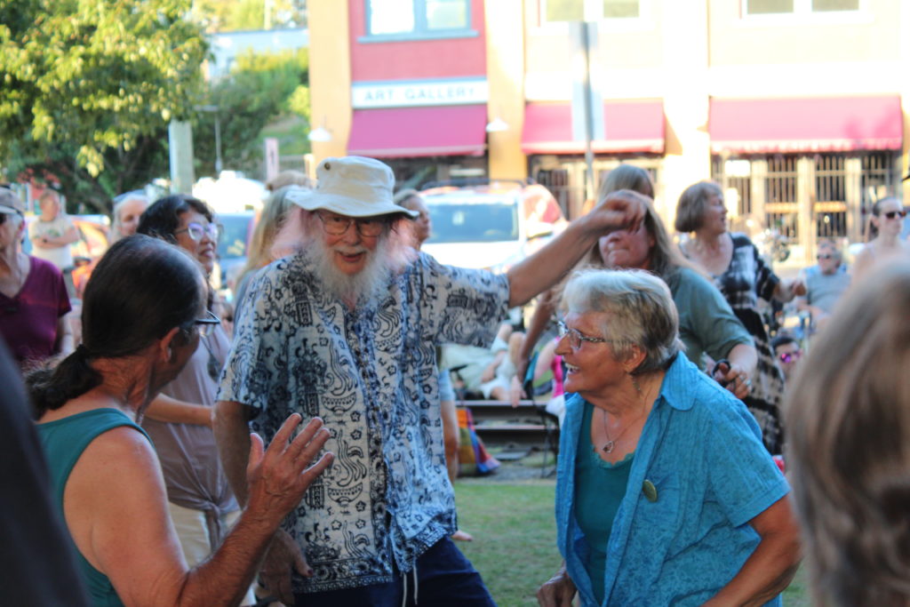 An older man dances with two women in an outdoor crowd.