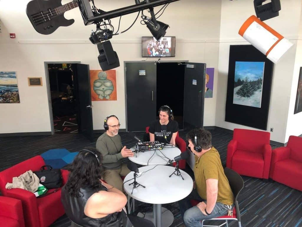 Four people gather around a round table with microphones and headsets.