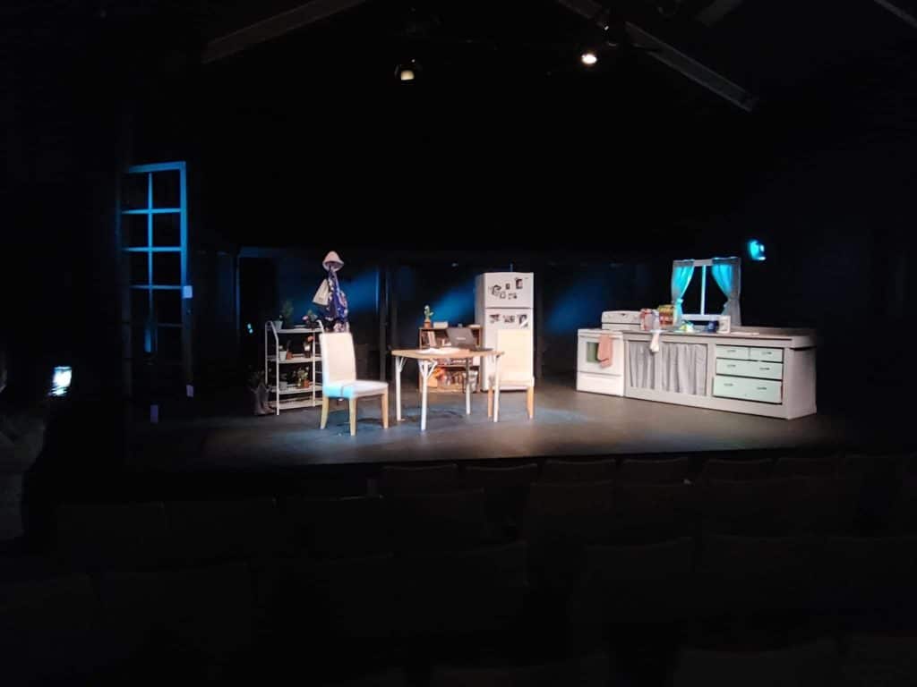 An image of a stage shows lights and a set with a kitchen scene.