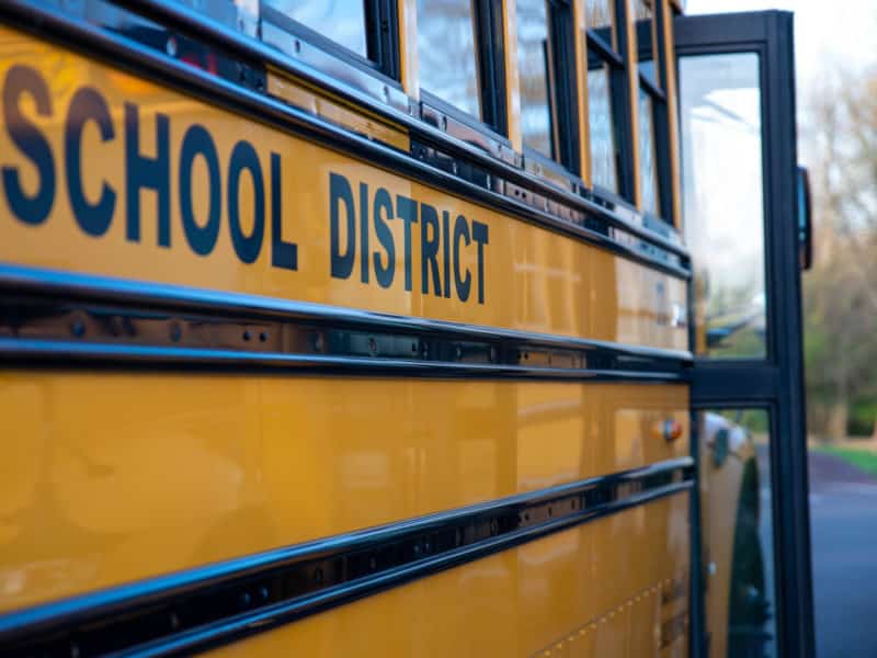 School District written on the side of a school bus. Door is open. No people, nature background.