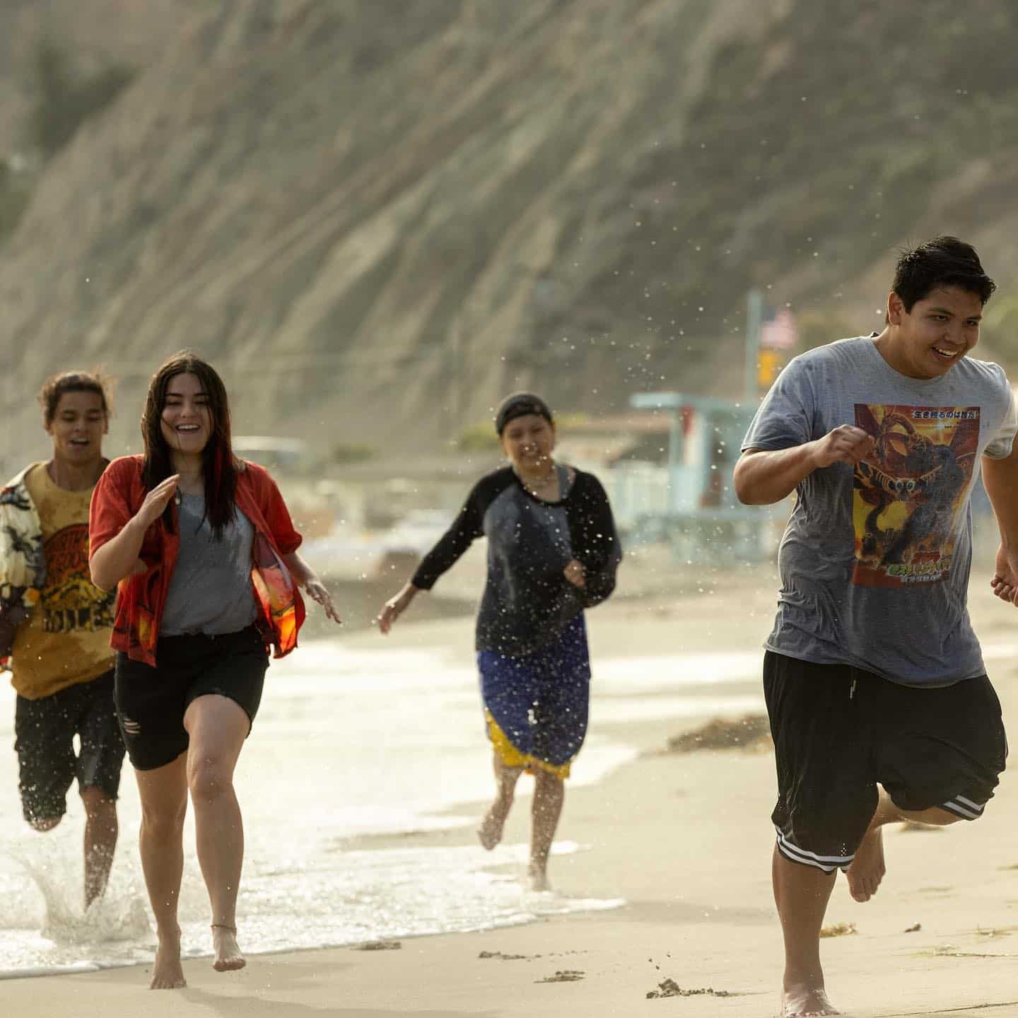 Four teens run joyfully down a beach