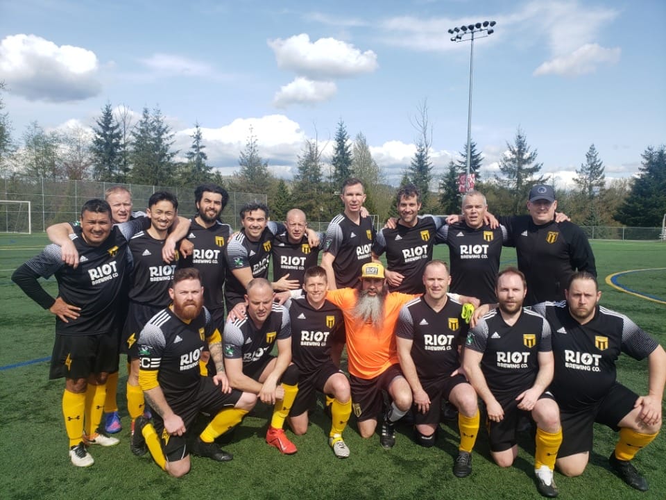 A team soccer photo, with the team standing on a field and smiling in their uniforms.