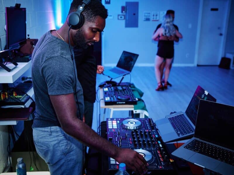 A DJ spins with a lap top and headphones in blue lights.