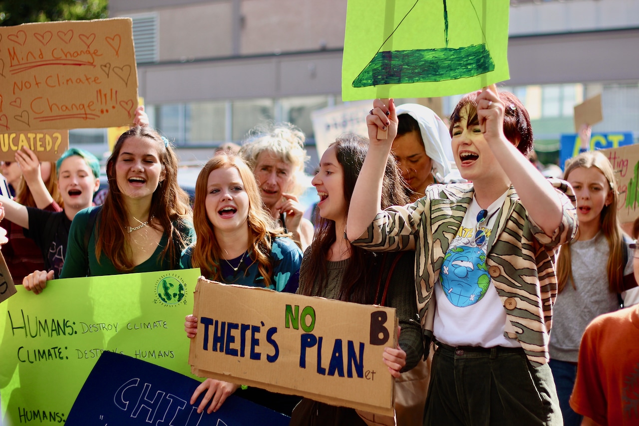 Four young people stand in front of a crowd holding protest signs