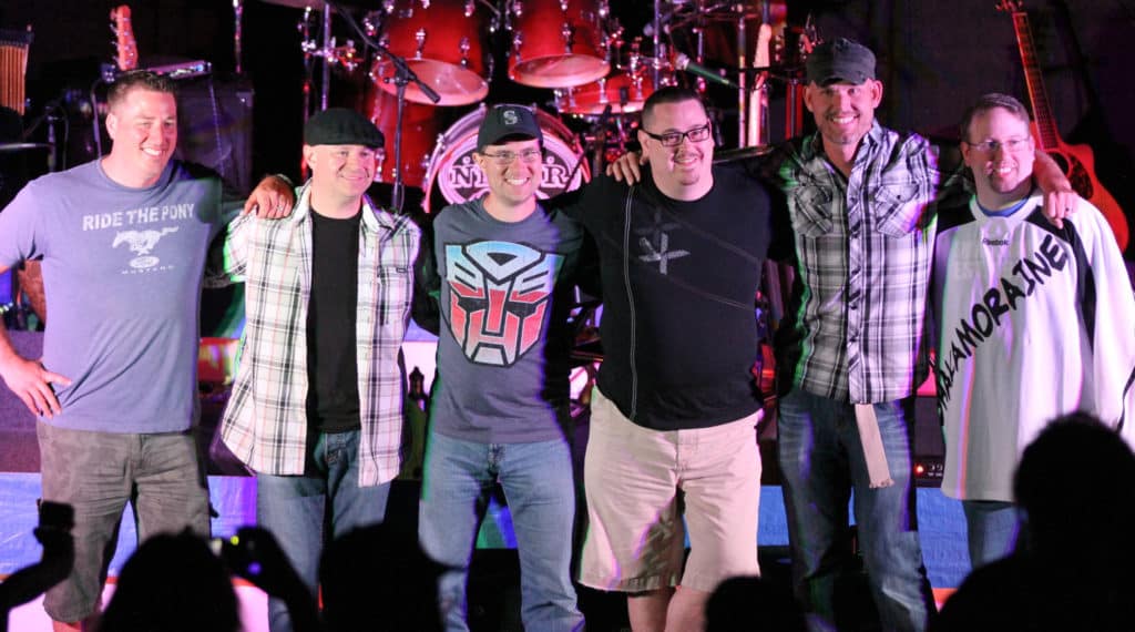Shakamoraine band members stand in a row facing camera with blue and purple lights.