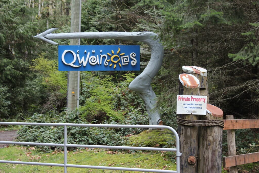 A photo of the Camp Qwanoes sign, located at the front gate of the camp. A "no trespassing" sign is posted next to it stating that it is private property.