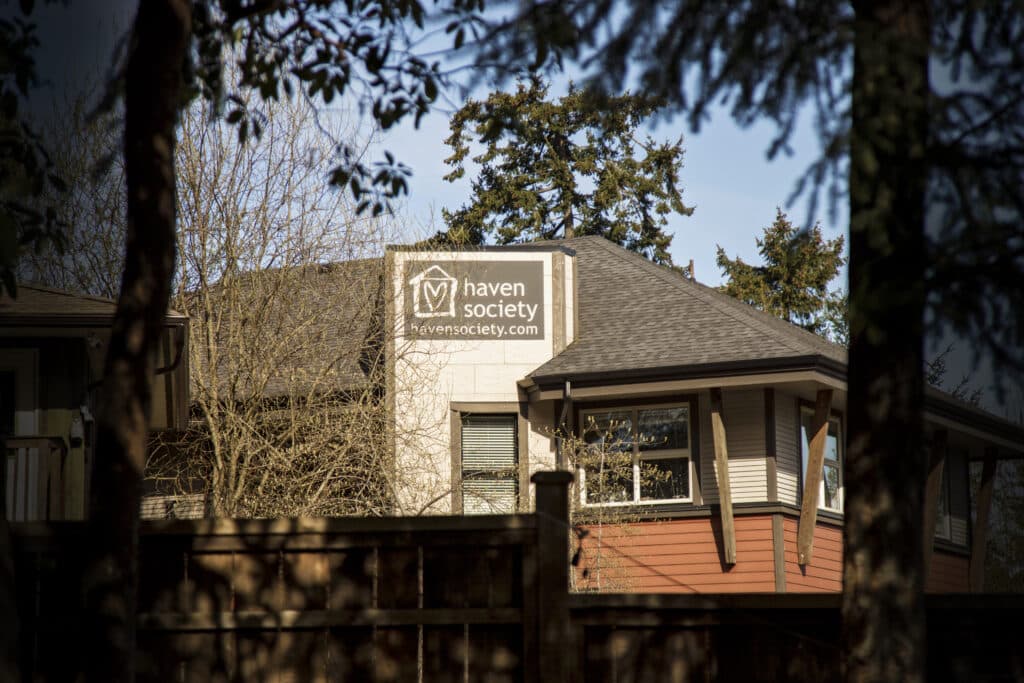 The front entrance of Haven Society framed in shadow by two trees.